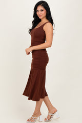 woman wearing a brown sleeveless ruched midi dress with a flared skirt and white high-heeled sandals