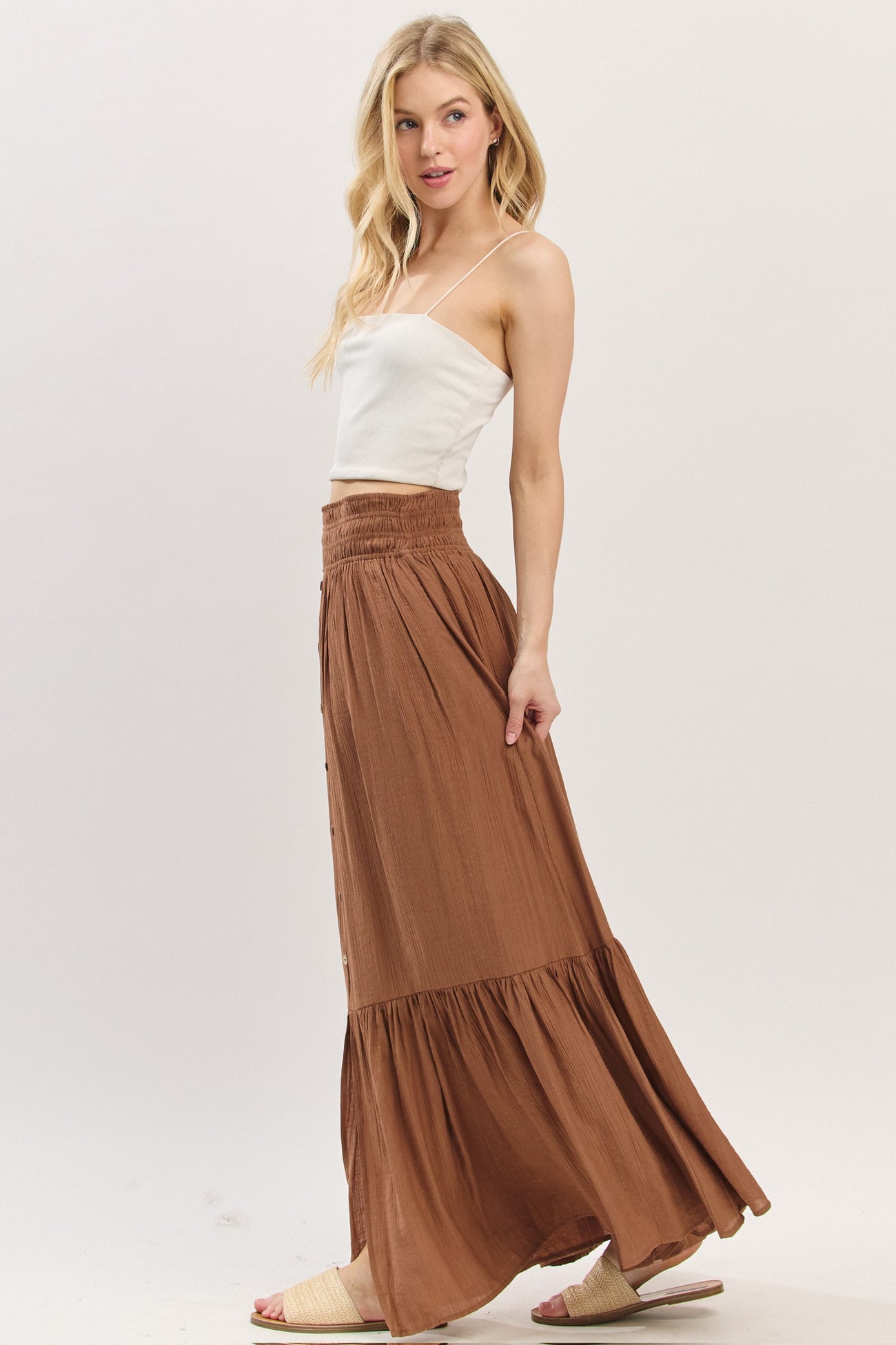woman wearing a white fitted crop top and a flowy brown maxi skirt with a tiered hem