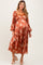 woman wearing a rust floral print maternity dress with puff sleeves and a flowing skirt, showcasing her baby bump