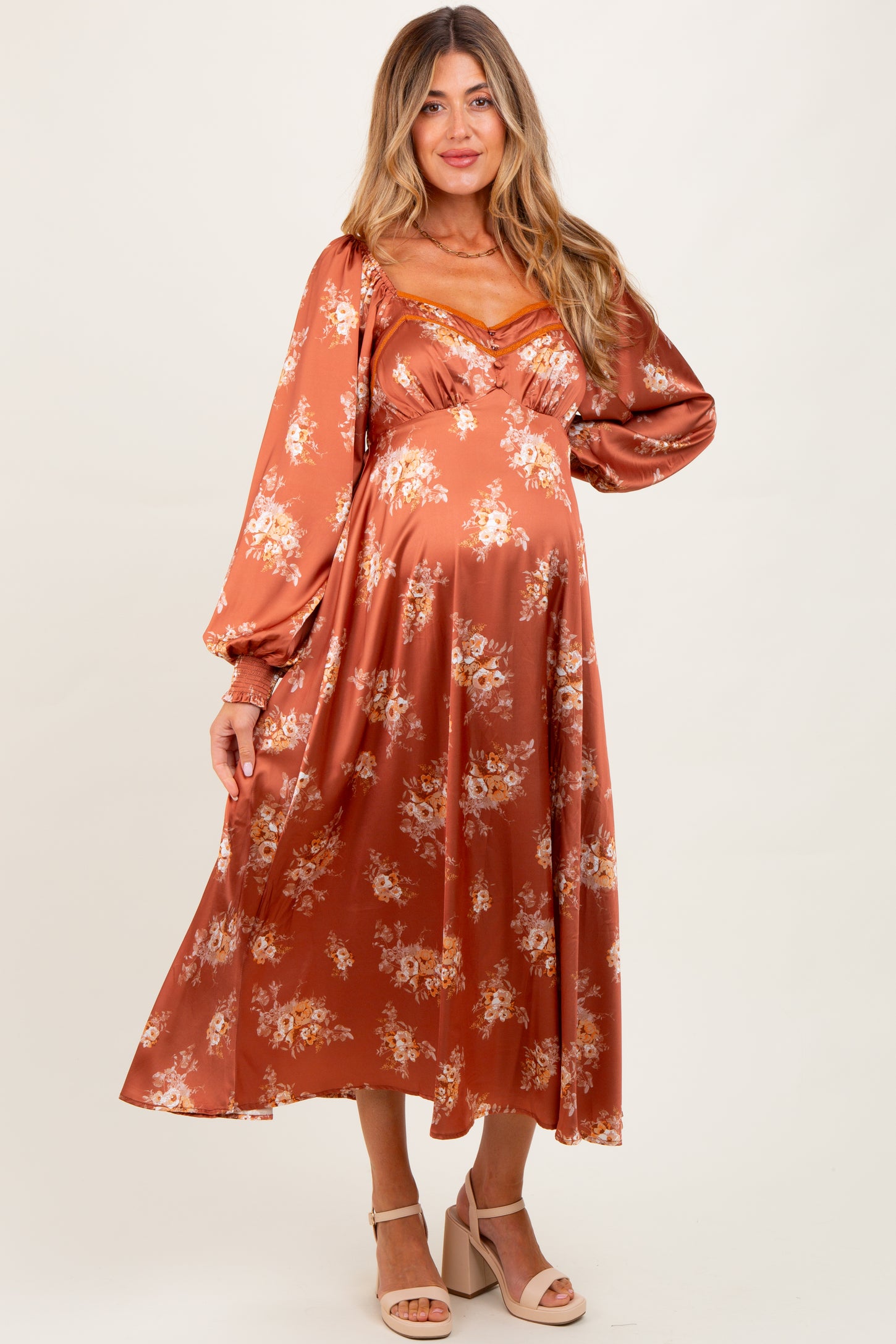 woman wearing a rust-colored floral maternity dress with long sleeves and a fitted bodice, highlighting her baby bump