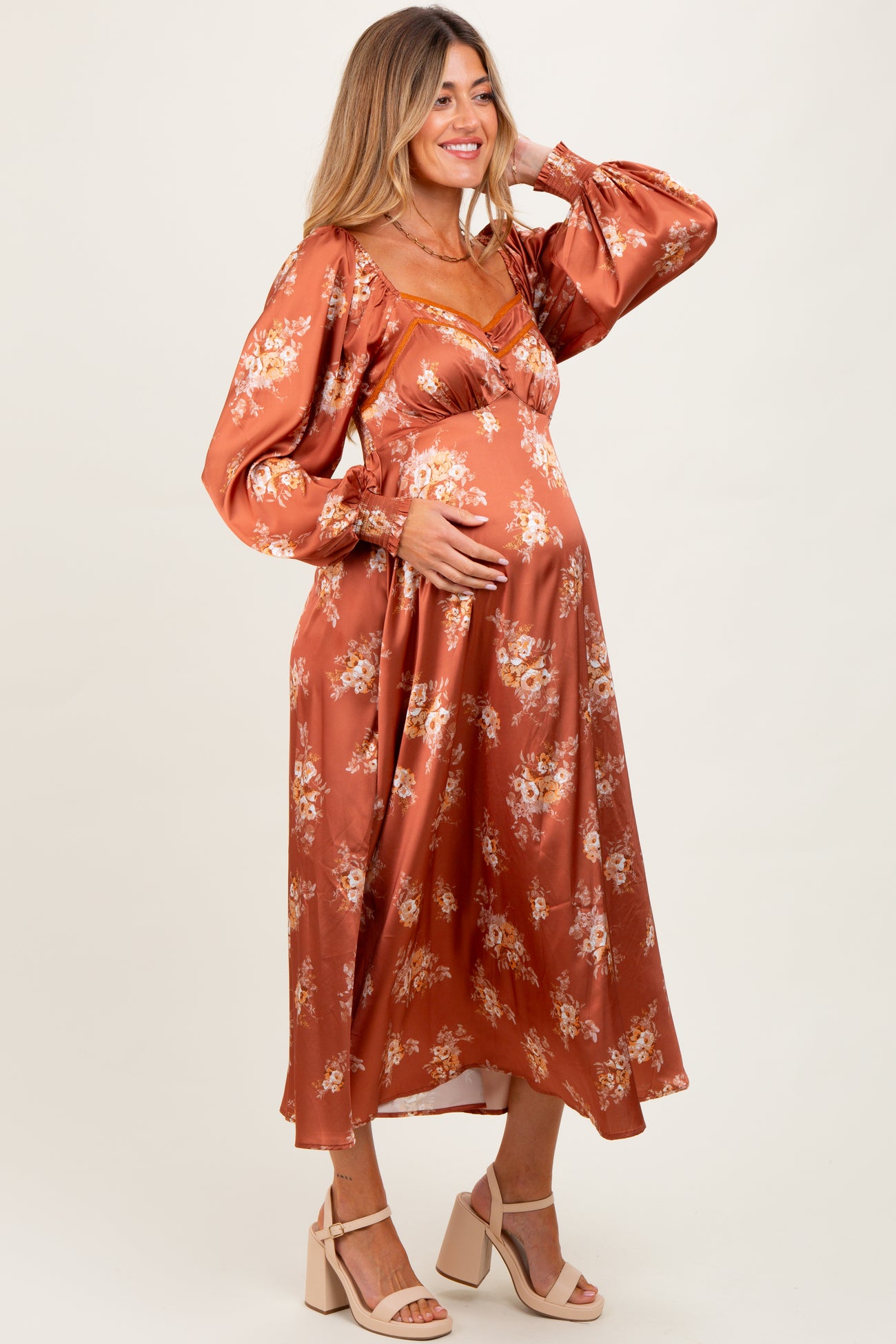 woman wearing an orange floral maternity dress with long sleeves and a v-neck, gently cradling her baby bump