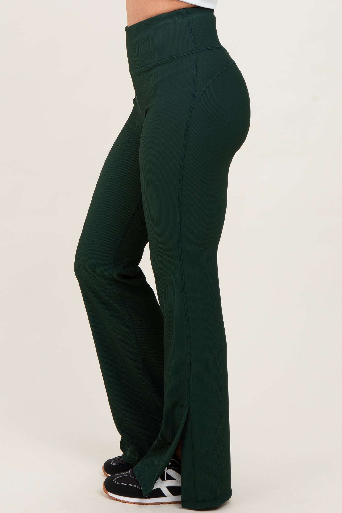 woman wearing high-waisted dark green flared workout pants with side slits and black athletic shoes