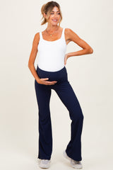 woman wearing a white maternity bodysuit and navy ribbed maternity pants, holding her baby bump