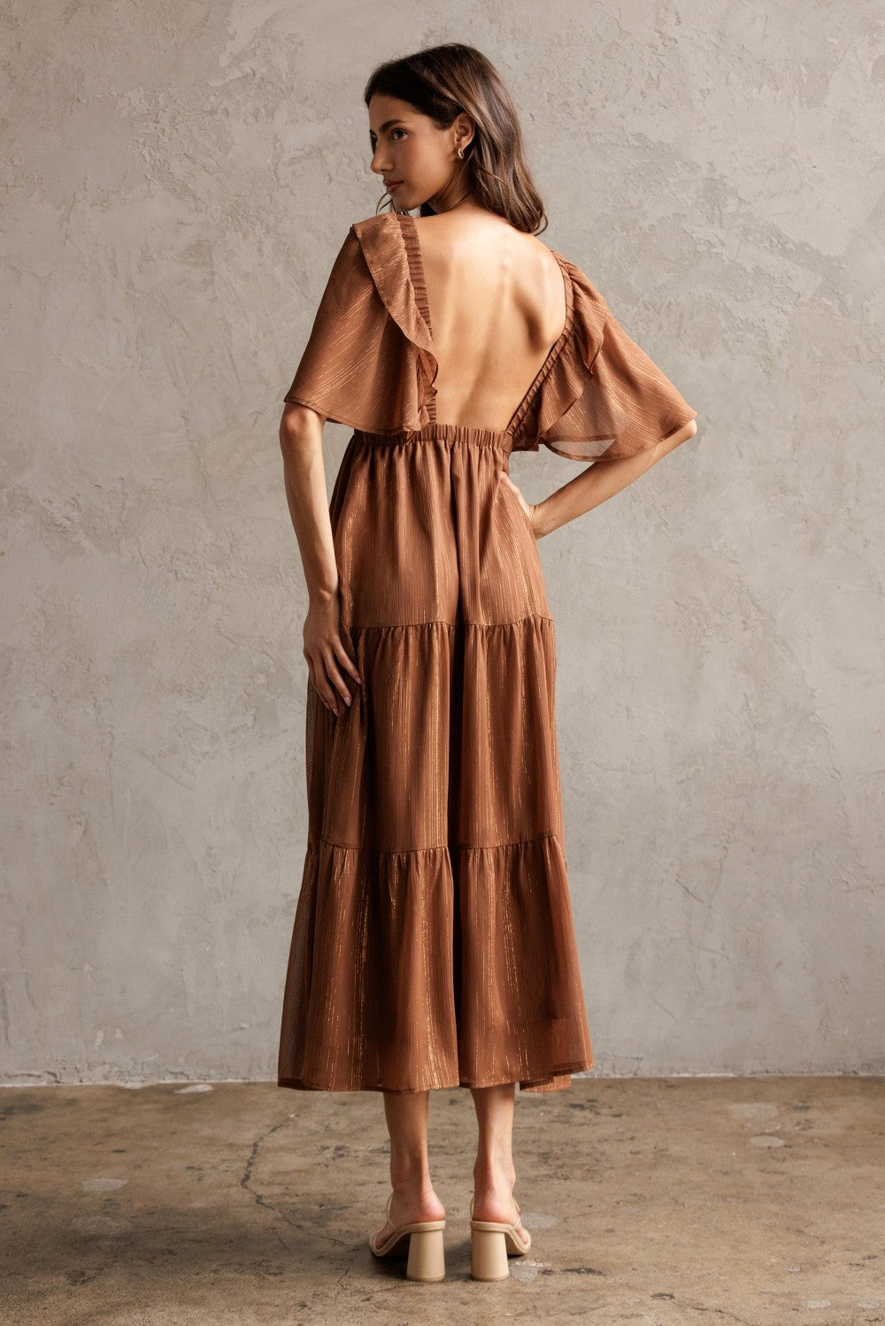 woman wearing a backless rust-colored maxi dress with ruffle sleeves and tiered skirt