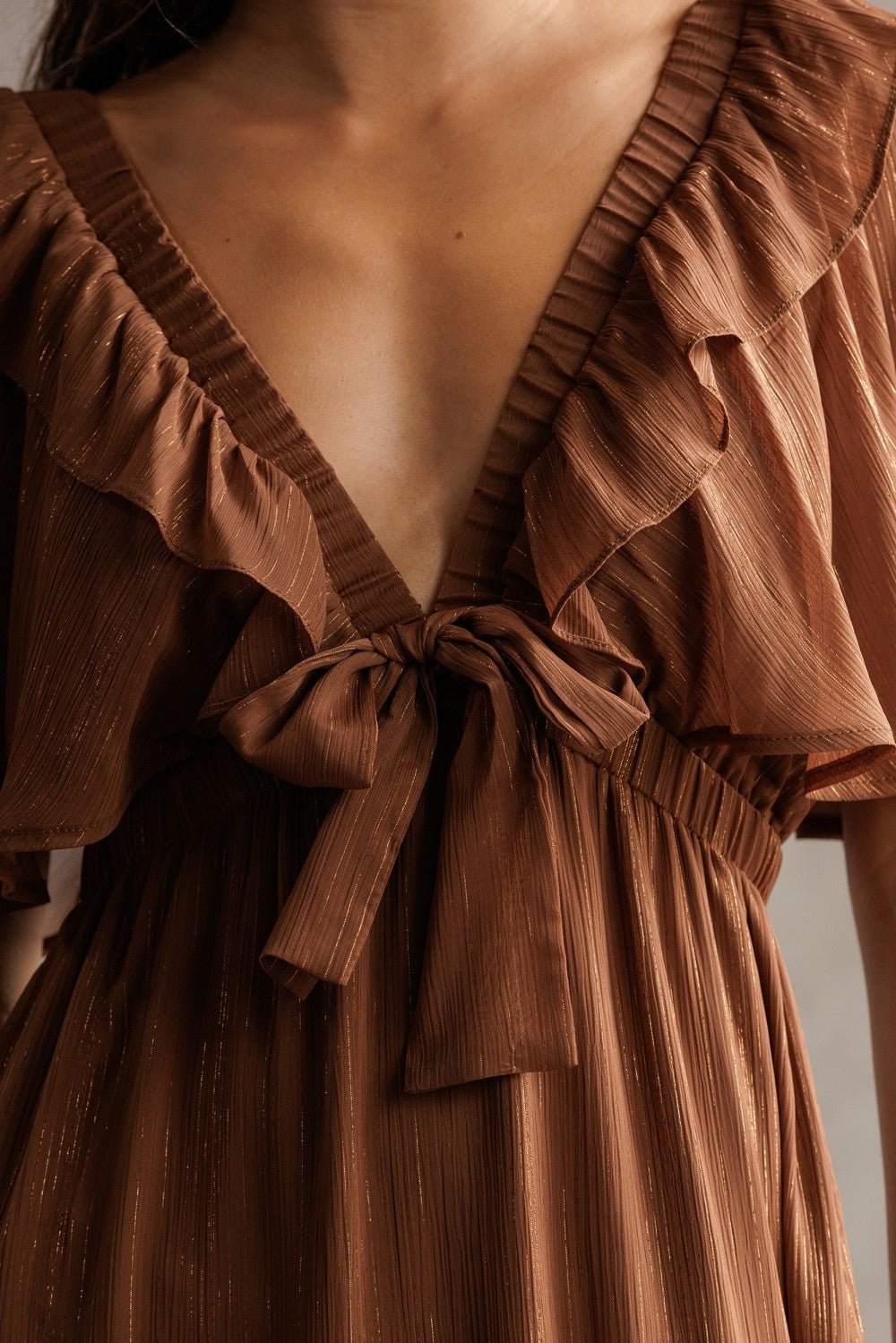woman wearing a rust brown dress with ruffled sleeves and a deep V-neck, accentuated by a front tie detail