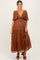 woman wearing a rust-colored tiered maternity dress with ruffled sleeves and a knotted front, showing her baby bump