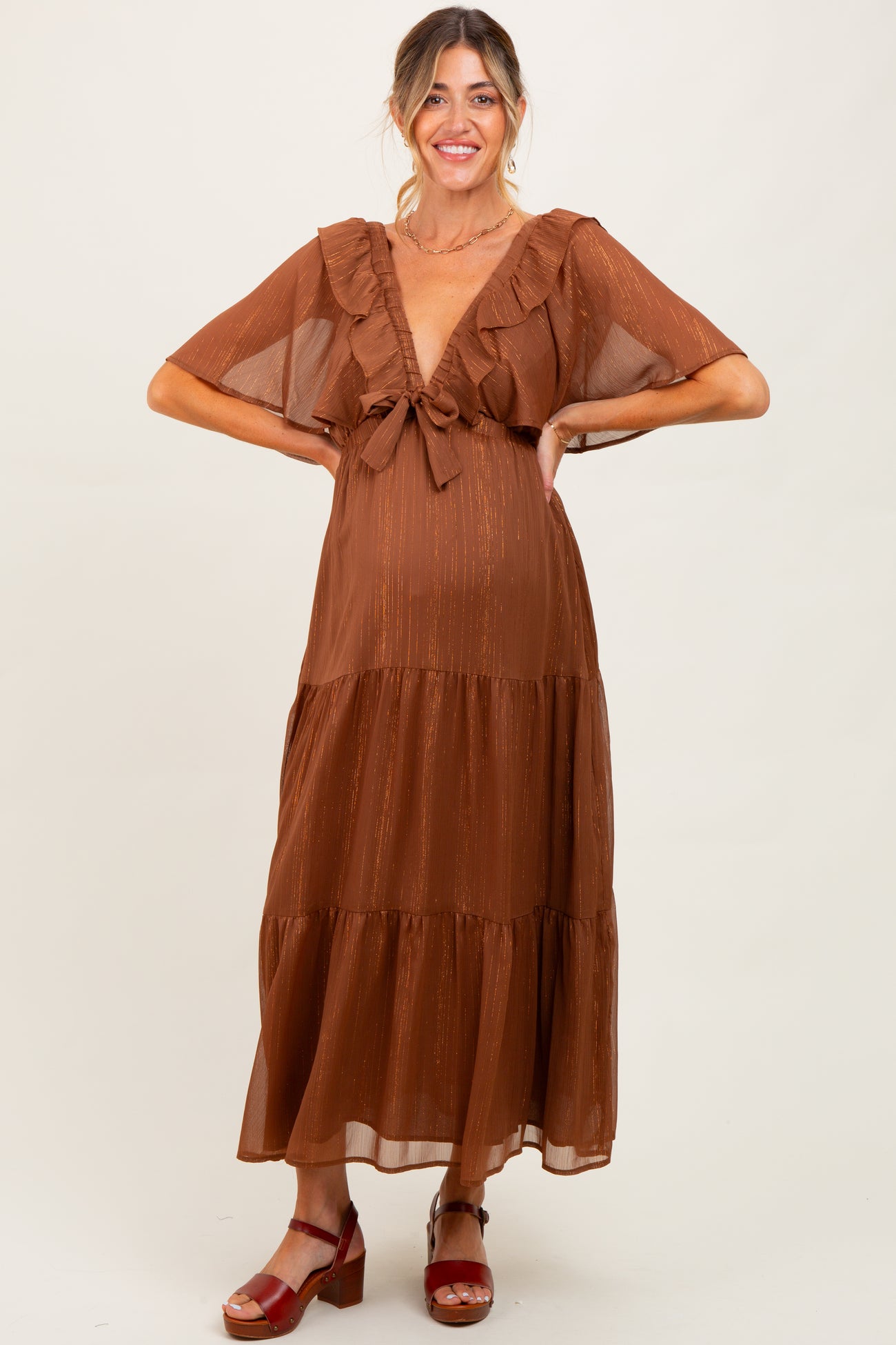 woman wearing a rust brown maternity maxi dress with ruffle sleeves and a tie front, showcasing her baby bump