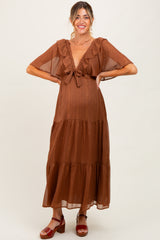woman wearing a rust brown maternity maxi dress with ruffle sleeves and a tie front, showcasing her baby bump