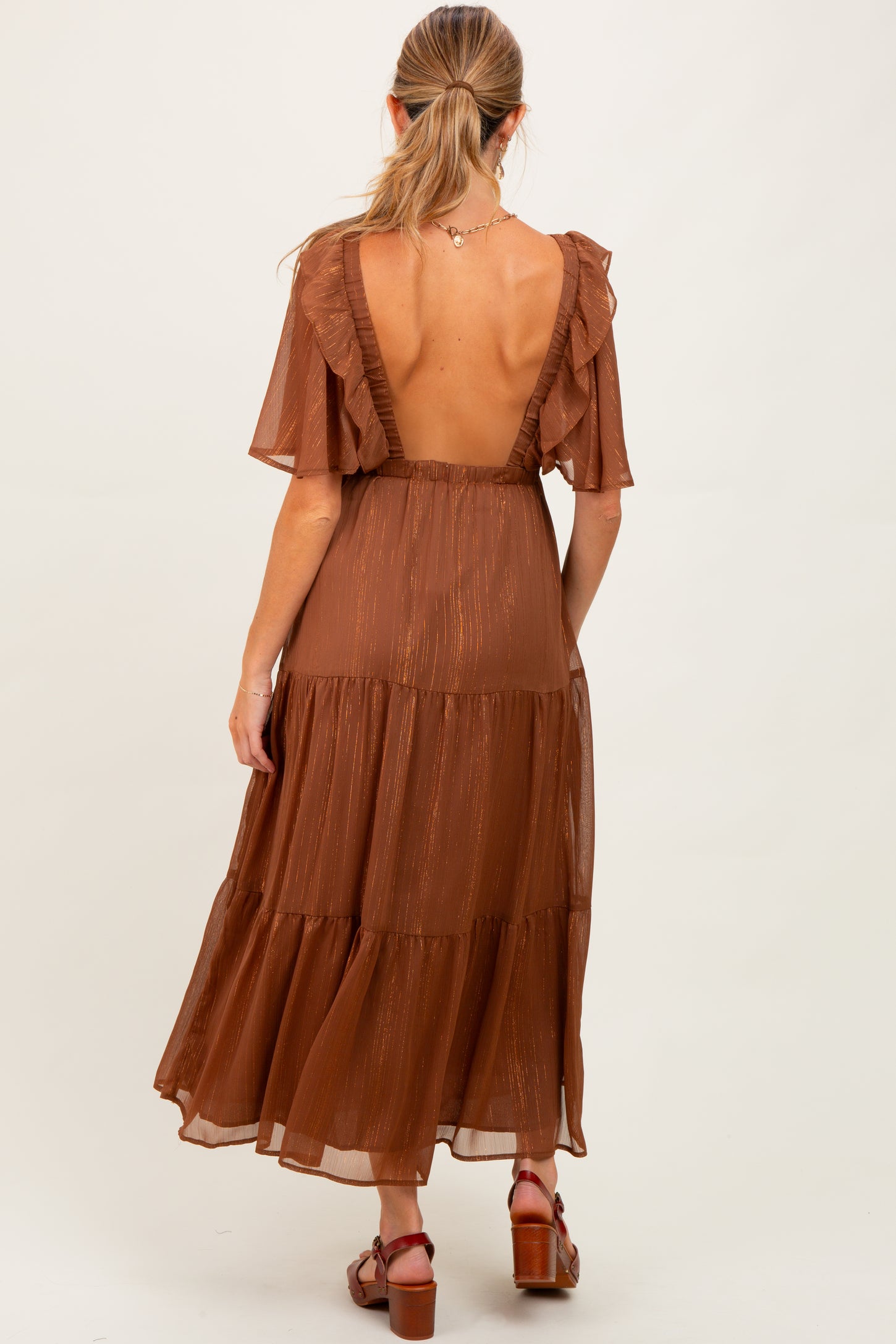 woman wearing a rust-colored maternity dress with flutter sleeves and a tiered design, showing her back