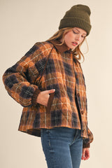 woman wearing a brown and navy plaid quilted jacket with a hood and a knit beanie, styled with jeans