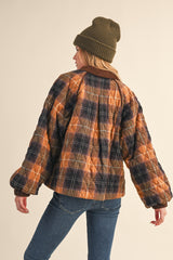 woman wearing a brown and navy plaid quilted jacket with oversized sleeves, styled with a green knit beanie
