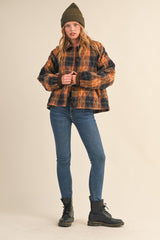 woman wearing a brown and black plaid cropped jacket with a green beanie, paired with skinny jeans and black combat boots