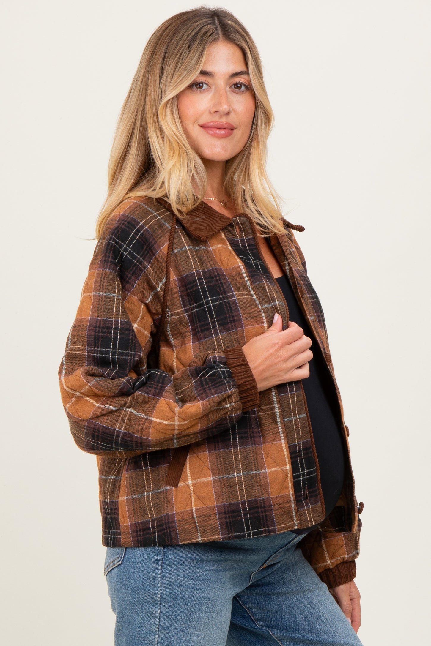woman wearing a brown plaid maternity jacket with a collar, styled with a black top and jeans, showing her baby bump