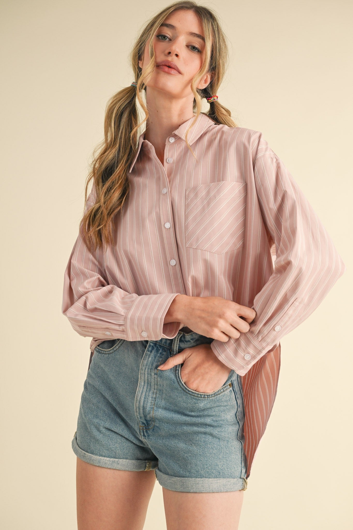 woman wearing a light pink striped button-up shirt with a pocket and high-waisted denim shorts