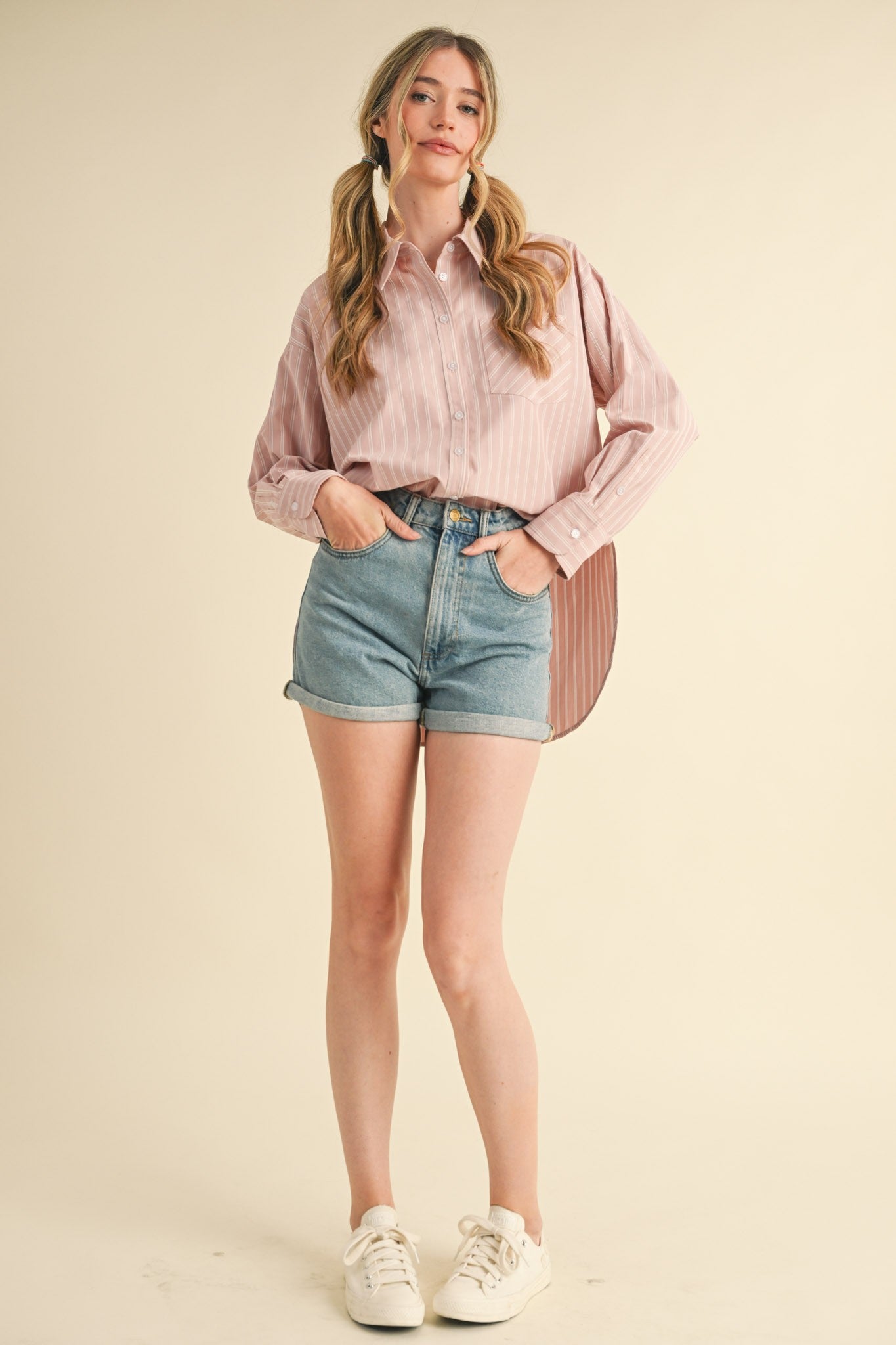 woman wearing a pink and white striped button-up shirt and high-waisted denim shorts with white sneakers