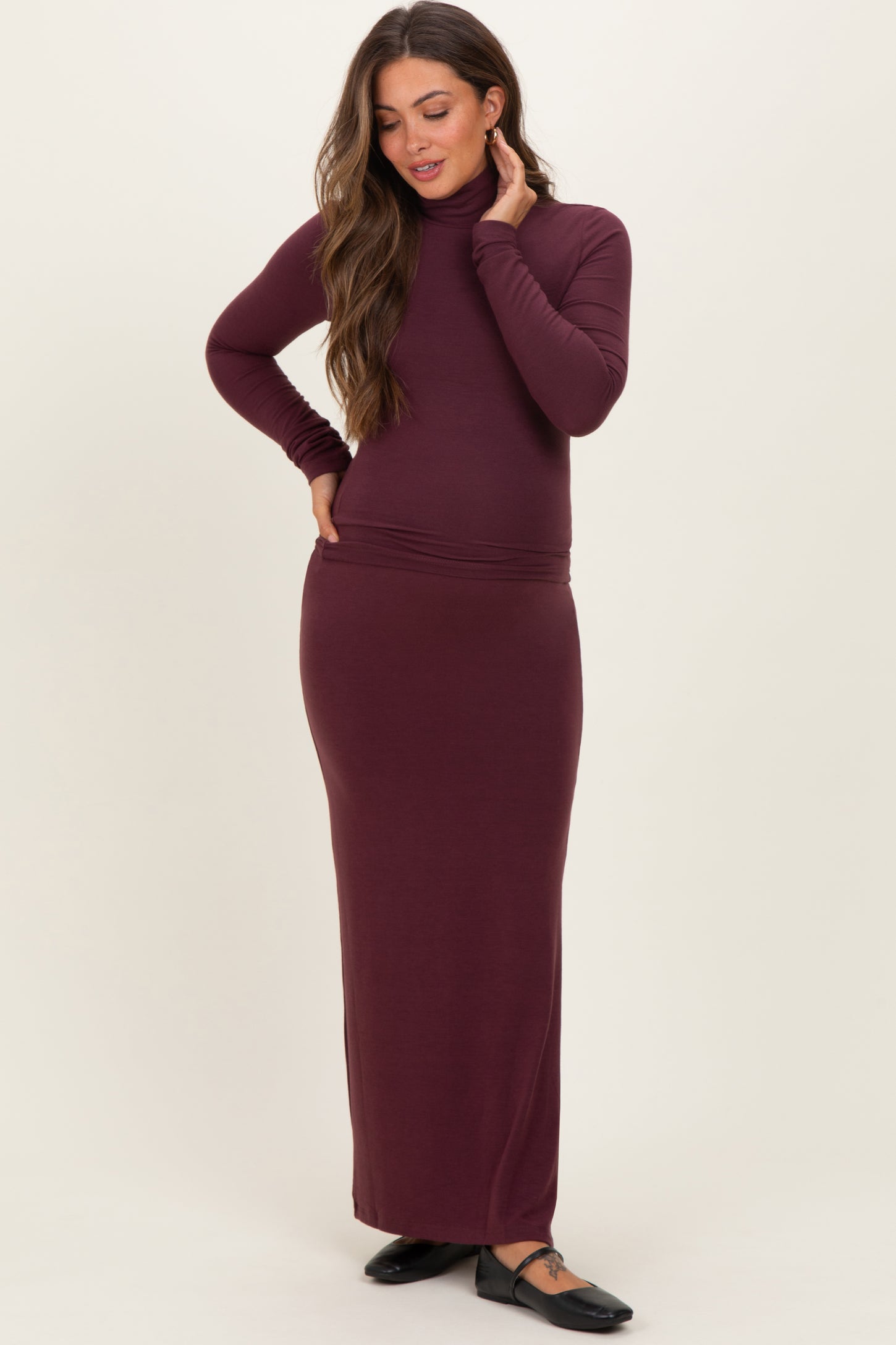 woman wearing a burgundy maternity turtleneck dress with a fitted silhouette and long sleeves, showcasing her baby bump