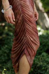 woman wearing a maroon ruched midi dress with a side slit and sheer fabric details