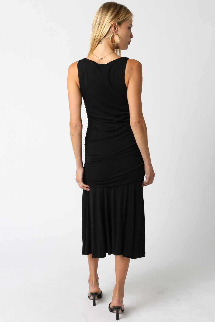 woman wearing a black sleeveless midi dress with ruched details and a flared skirt, shown from the back