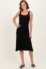 woman wearing a black sleeveless ruched dress with a flared skirt and black sandals