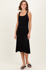 woman wearing a black sleeveless ruched maxi dress with a flared skirt and black slide sandals