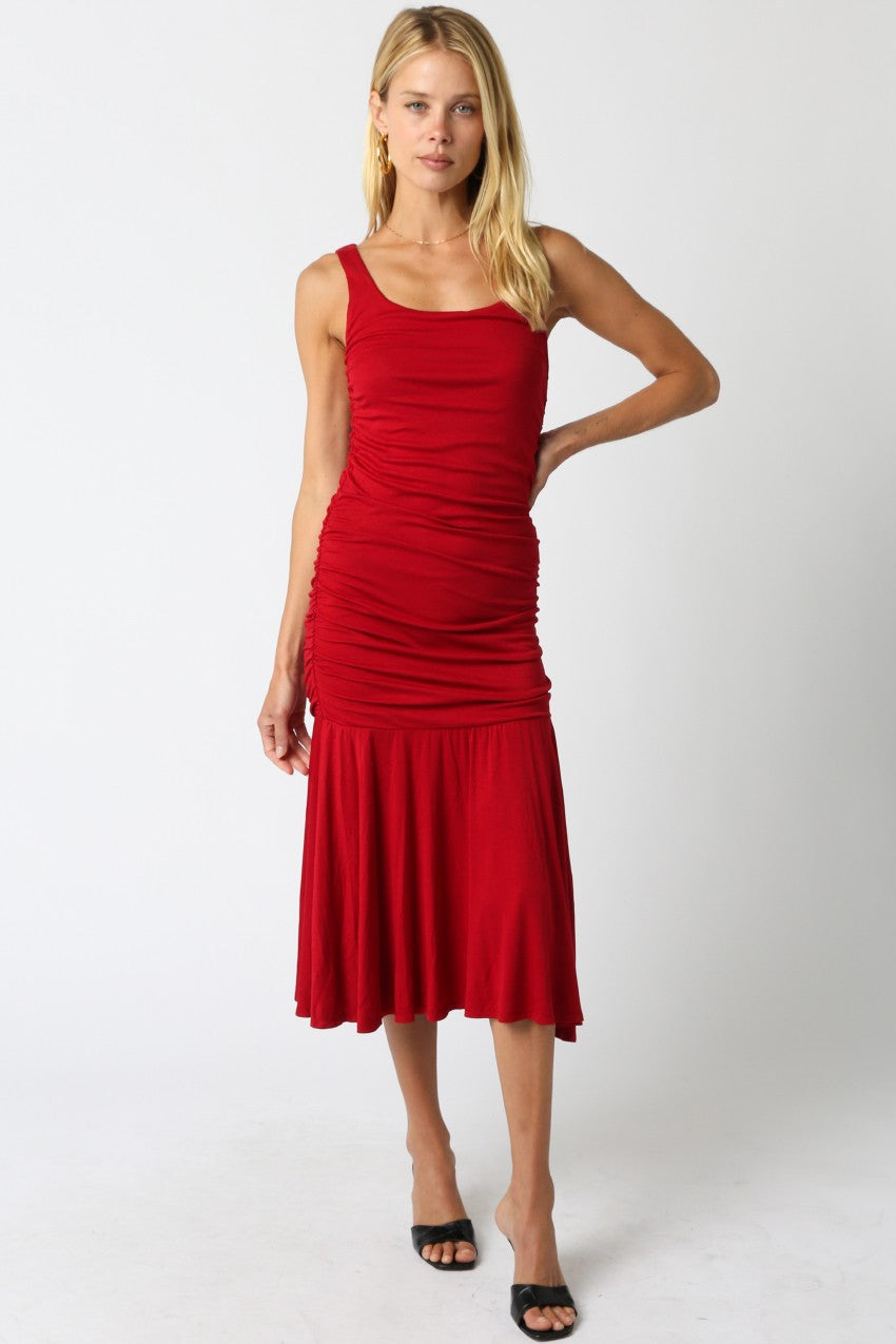 woman wearing a red fitted midi dress with ruched detailing and a flared hem, standing in a relaxed pose