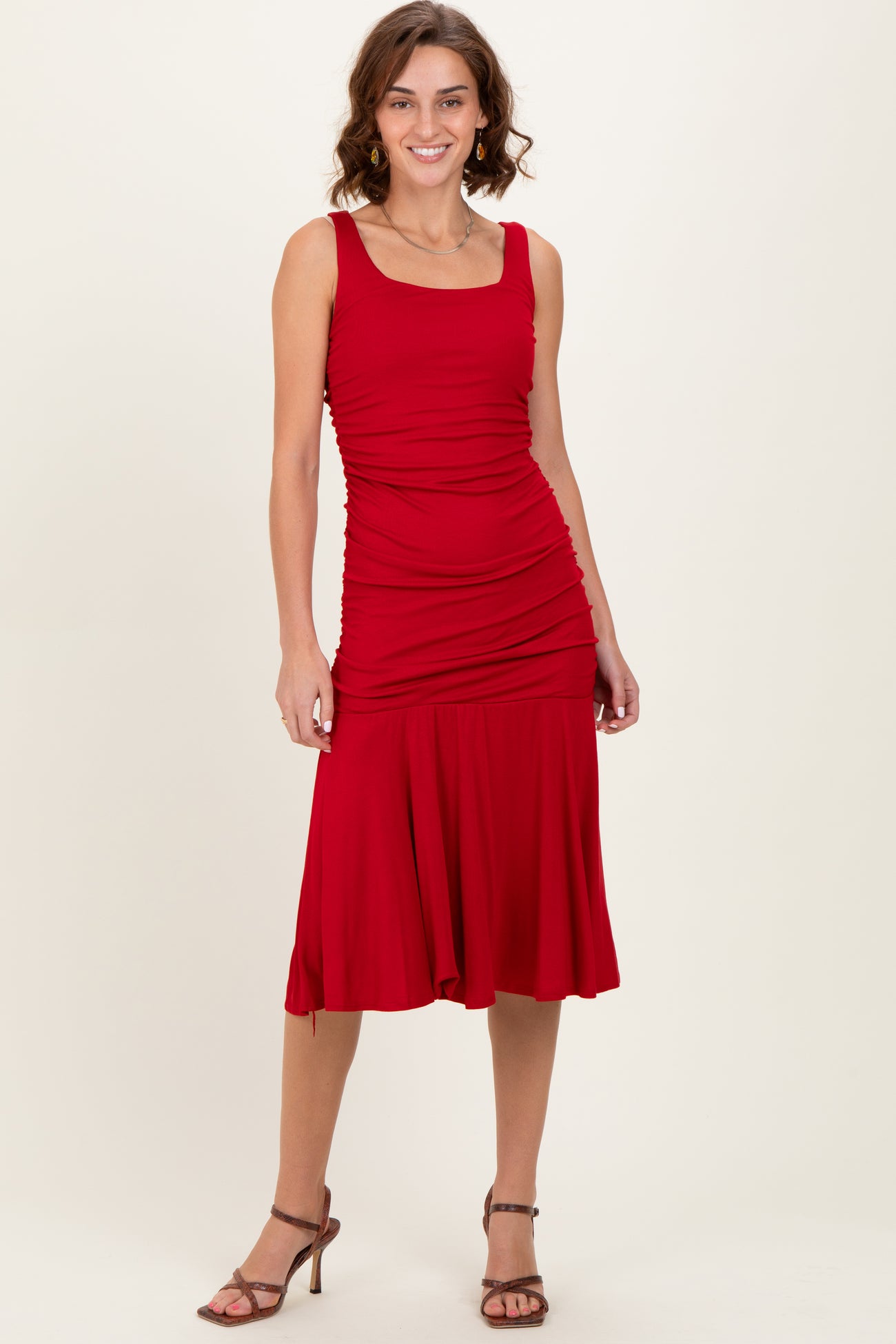 woman wearing a red fitted midi dress with ruching details and a flared hem, paired with strappy heels