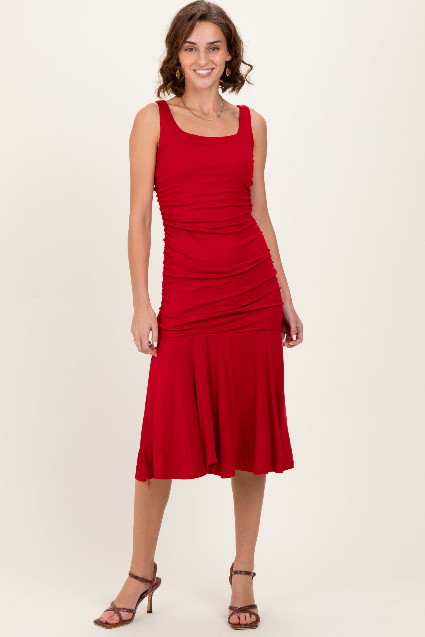 woman wearing a red fitted midi dress with ruching details and a flared hem, paired with strappy heels