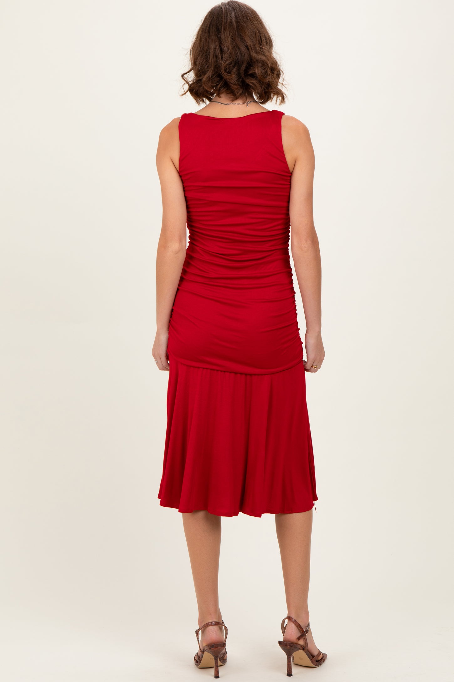 woman wearing a red fitted sleeveless dress with ruching and a flared hem, shown from the back