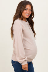 woman wearing a light pink ribbed maternity sweatshirt, showing her baby bump, paired with denim jeans