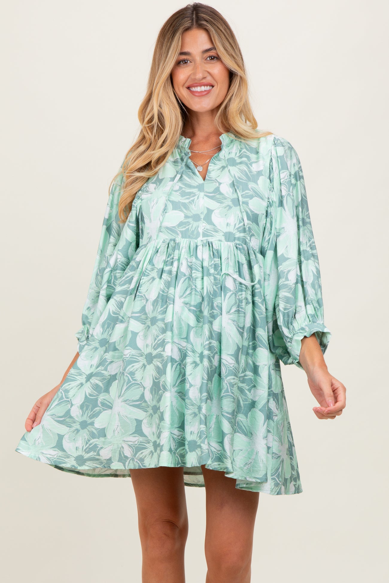 woman wearing a green floral maternity dress with a relaxed fit and balloon sleeves, showcasing a baby bump