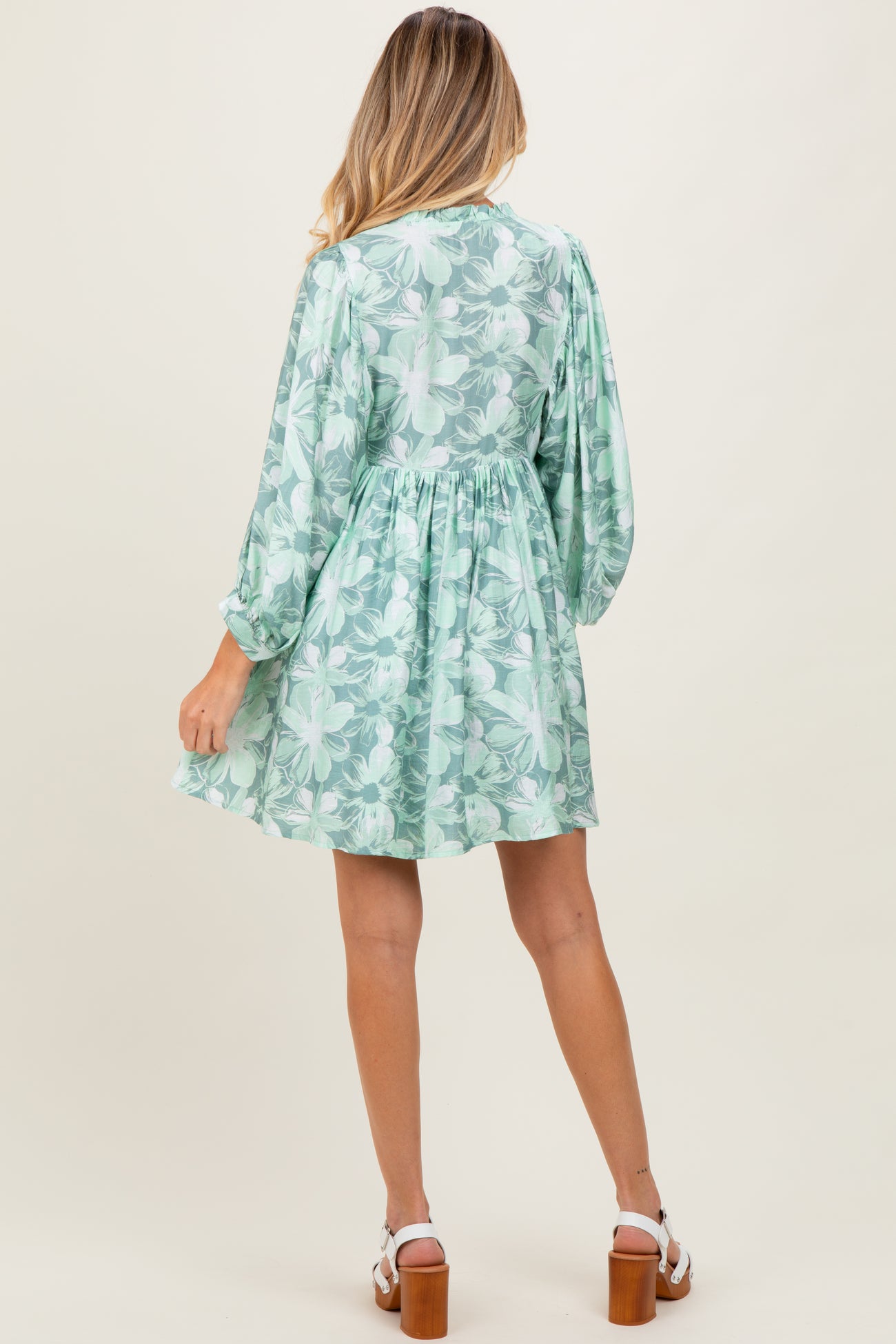 woman wearing a floral green maternity dress with long sleeves and a gathered waist, showing a baby bump from the back