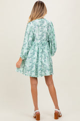 woman wearing a floral green maternity dress with long sleeves and a gathered waist, showing a baby bump from the back