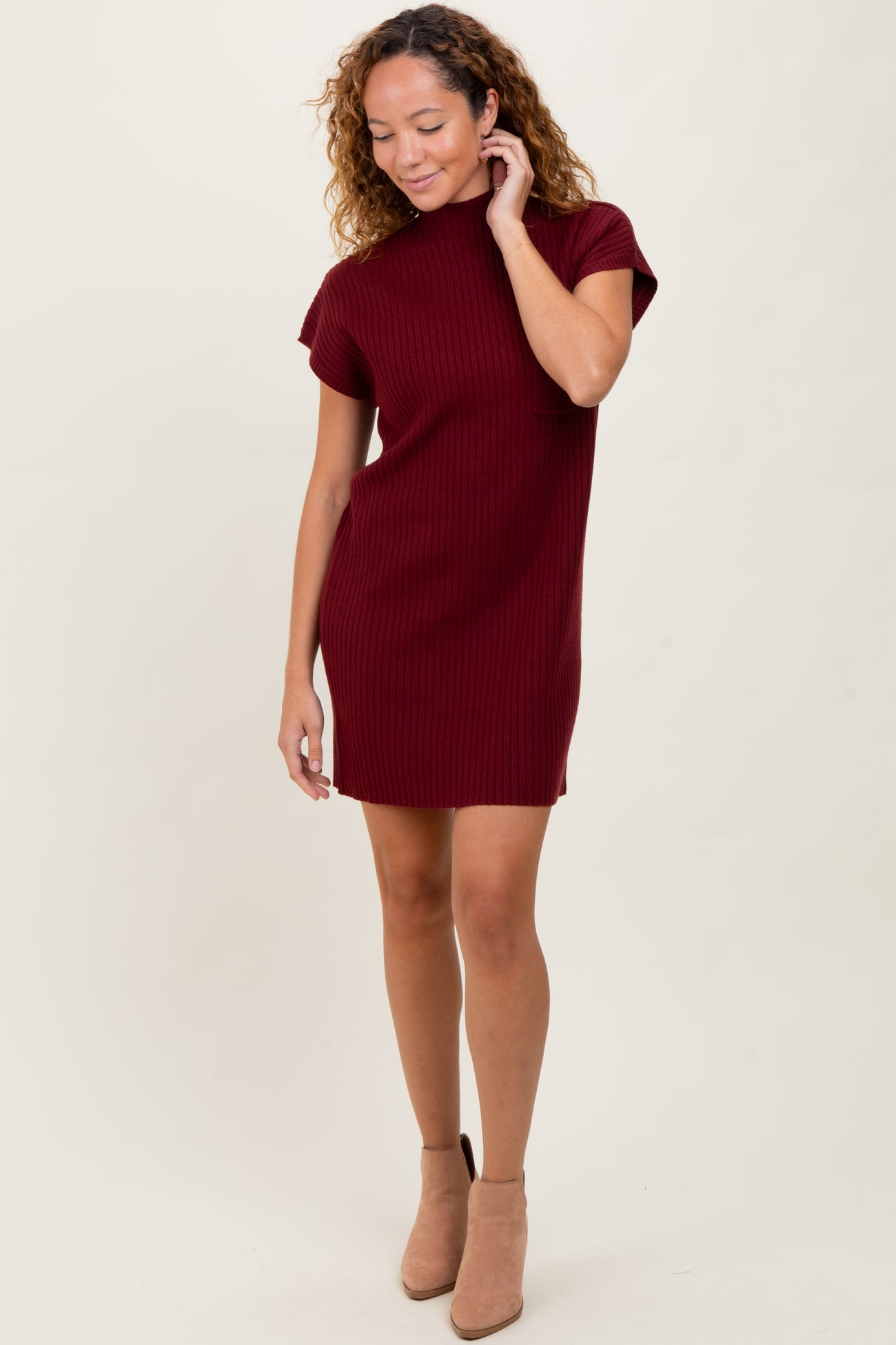 woman wearing a burgundy ribbed knit short sleeve dress with a high neckline and tan ankle boots