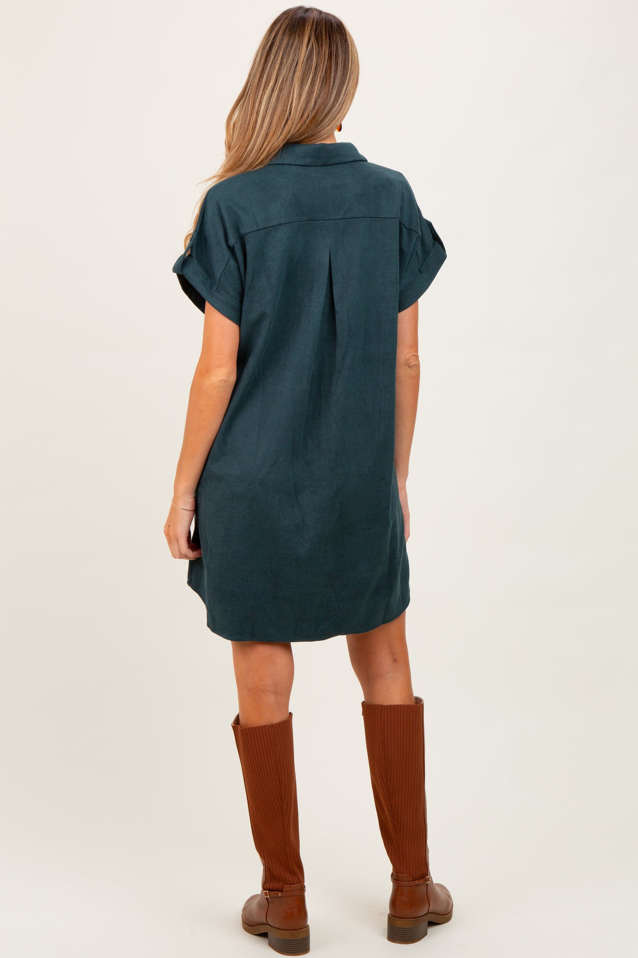 woman wearing a green maternity dress with rolled sleeves and a relaxed fit, standing with her back to the camera