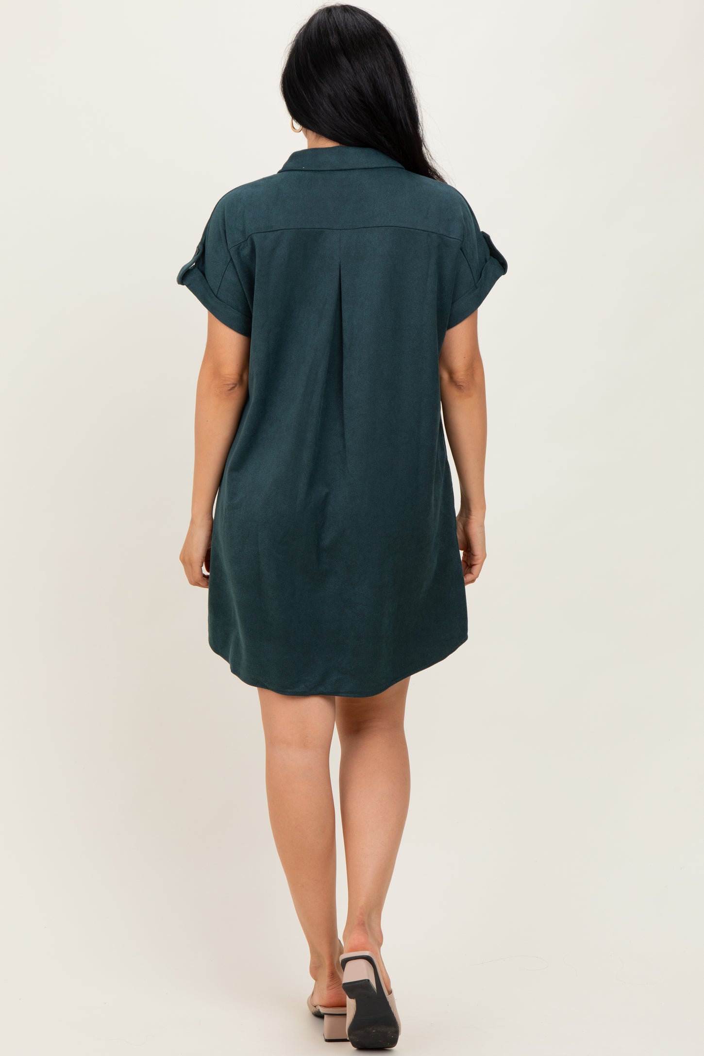 woman wearing a dark green short sleeve shirt dress with rolled sleeves and a relaxed fit, viewed from the back