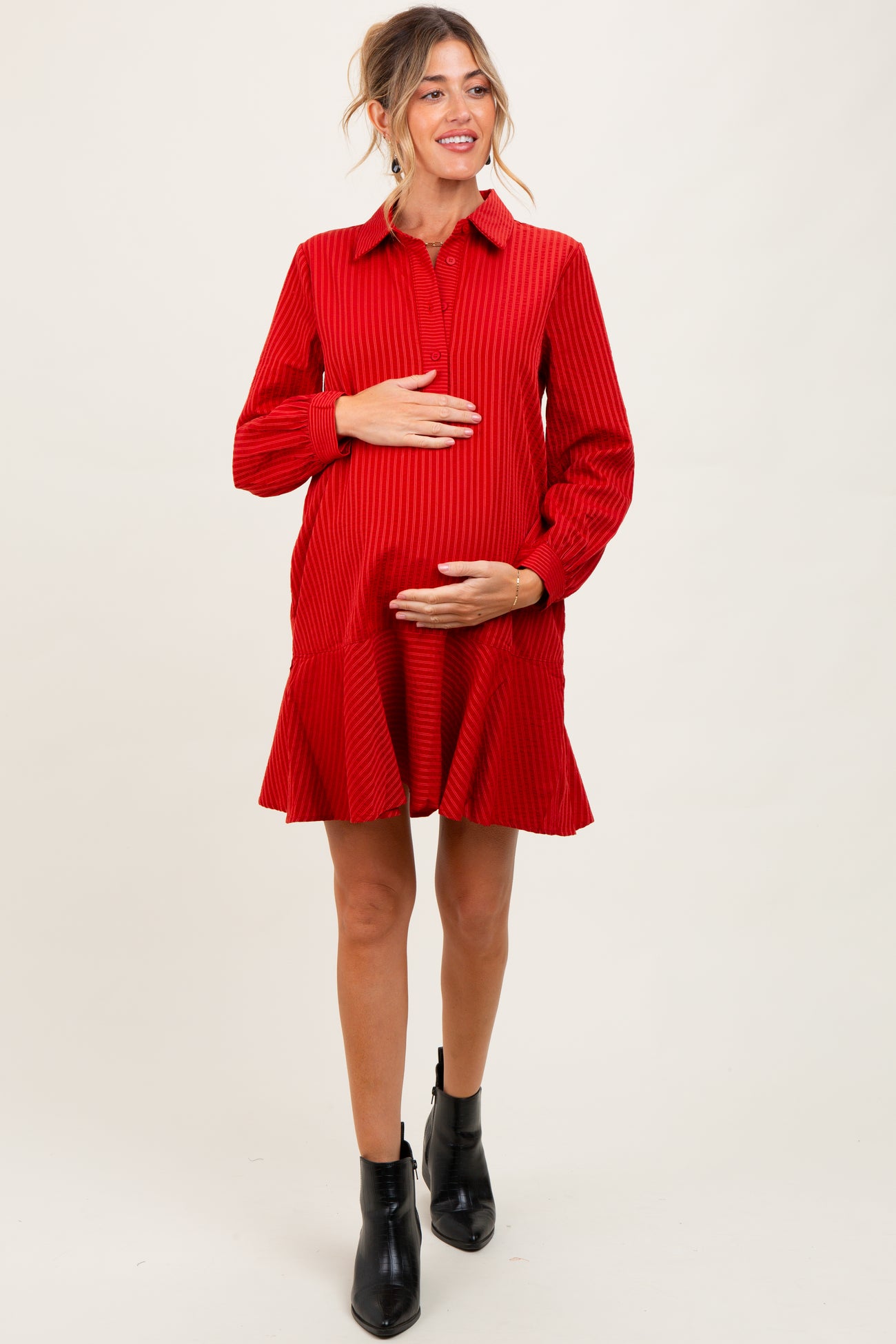 woman wearing a red corduroy maternity dress with a flared skirt and holding her baby bump