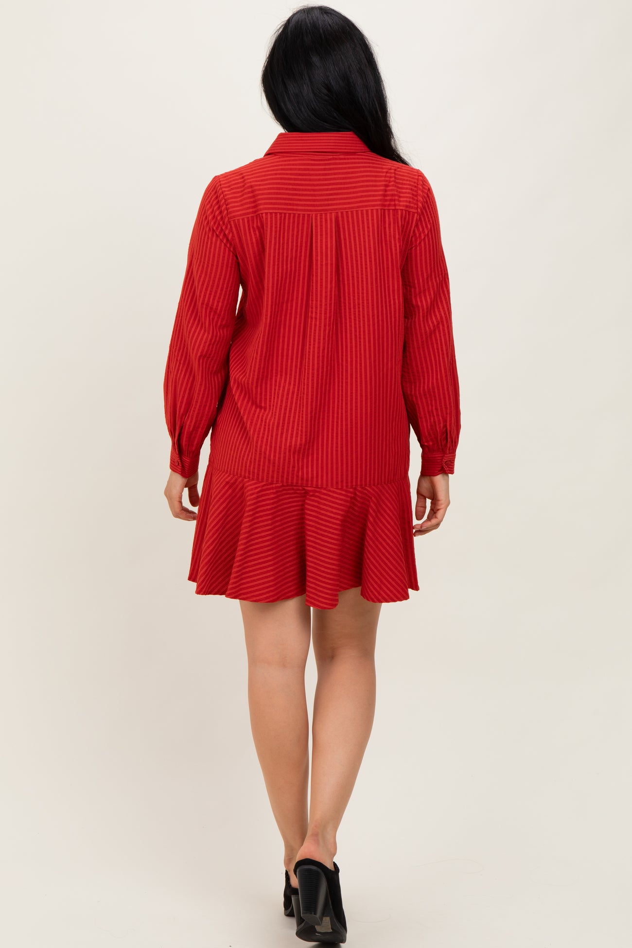 woman wearing a red long-sleeve striped dress with a ruffled hem and a button-up collar, shown from the back