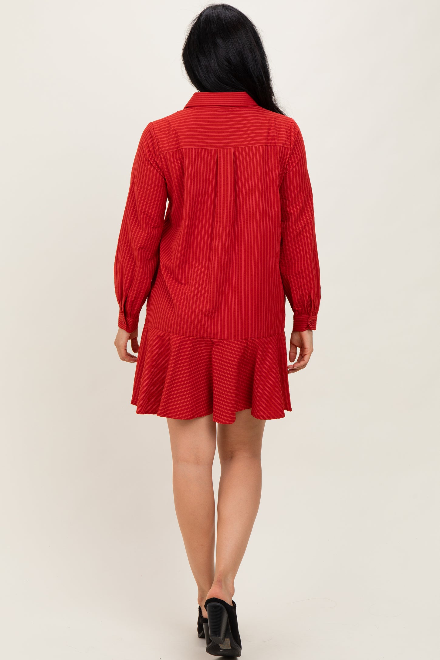 woman wearing a red long-sleeve striped dress with a ruffled hem and a button-up collar, shown from the back