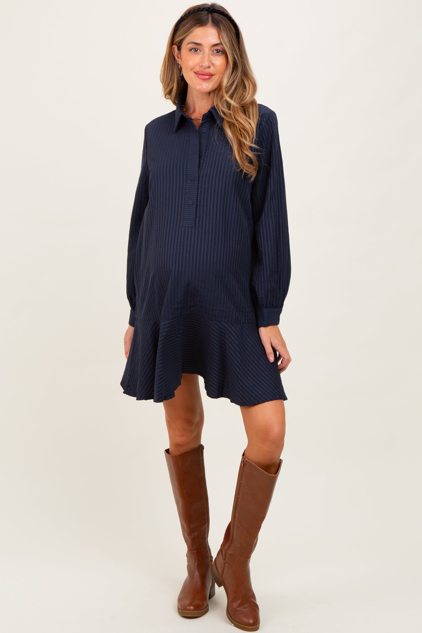 woman wearing a navy striped maternity shirt dress with a flared hem and brown knee-high boots, showing her baby bump