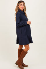 woman wearing a navy striped maternity dress with a flared skirt and brown knee-high boots, showing her baby bump