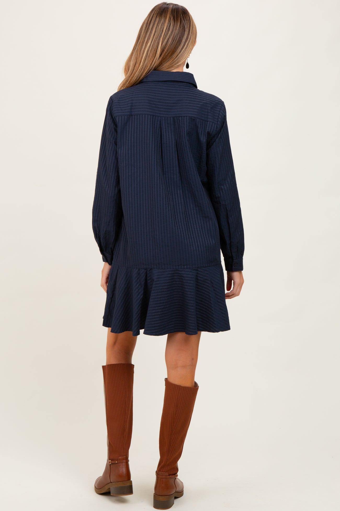 woman wearing a navy striped maternity dress with a ruffled hem and long sleeves, showing the back view