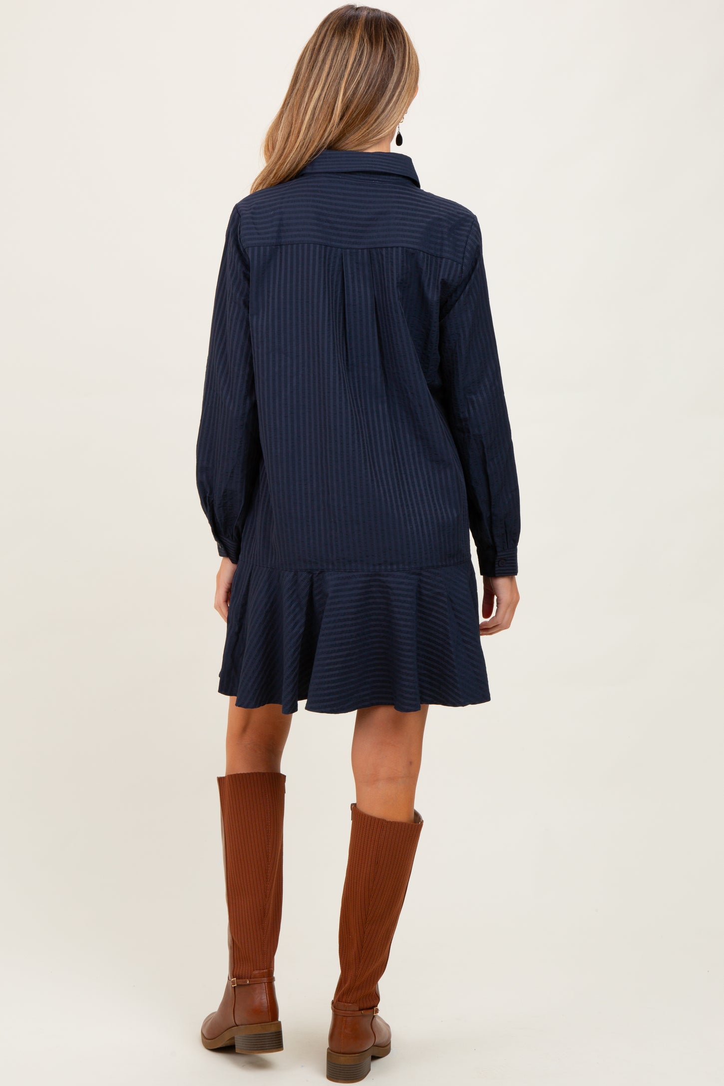 woman wearing a navy striped maternity dress with a ruffled hem and long sleeves, showing the back view