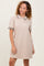 woman wearing a beige short sleeve polo dress with textured pattern and black trim details