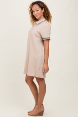 woman wearing a beige short sleeve dress with a textured pattern and decorative collar, styled with ankle boots