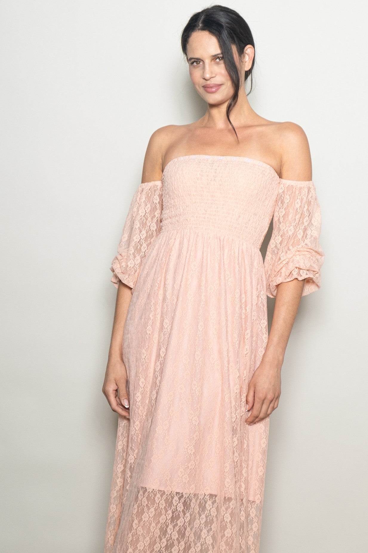 woman wearing a blush pink off-the-shoulder lace maxi dress with puff sleeves and a smocked bodice