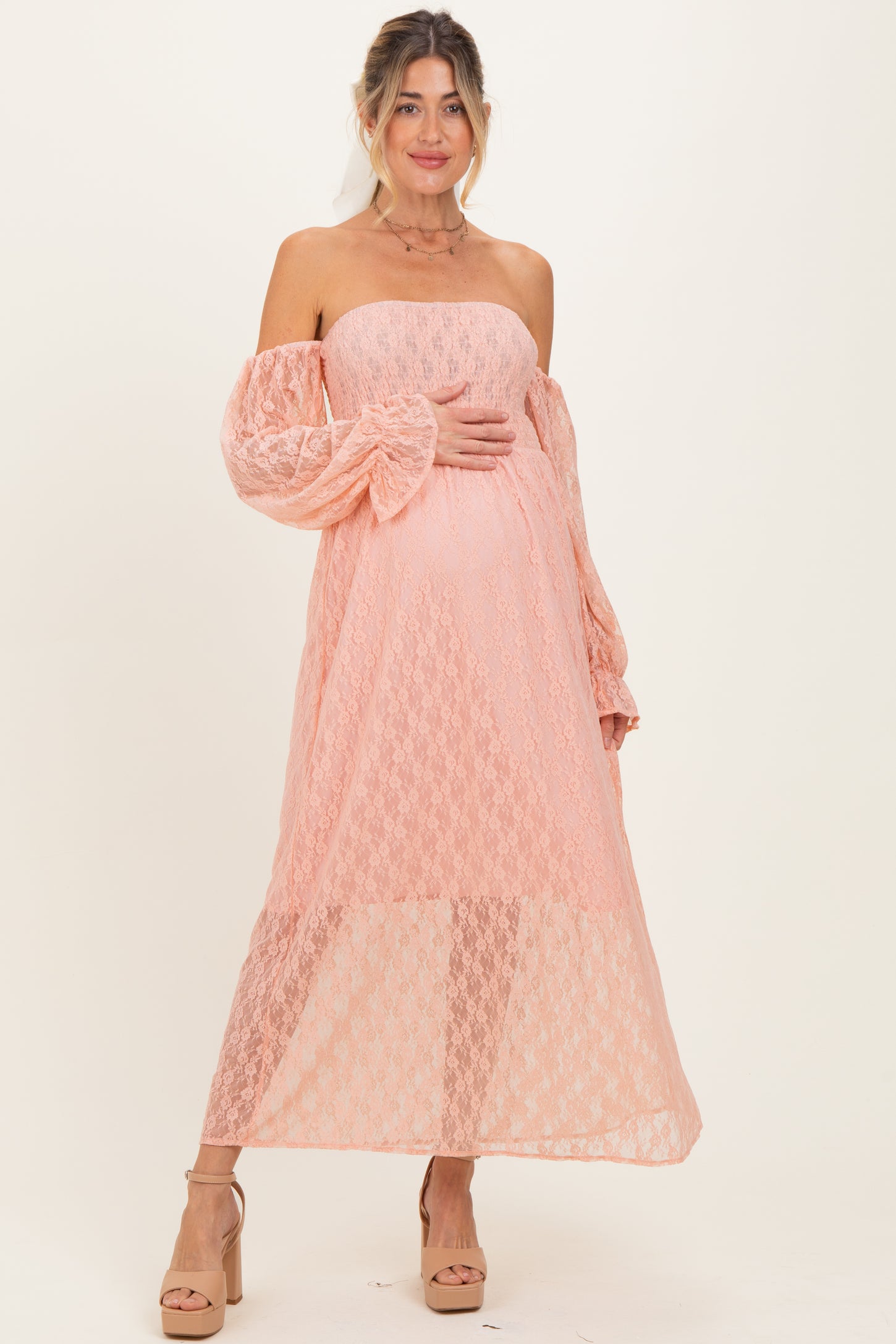 woman wearing a peach off-the-shoulder lace maternity dress and holding her baby bump