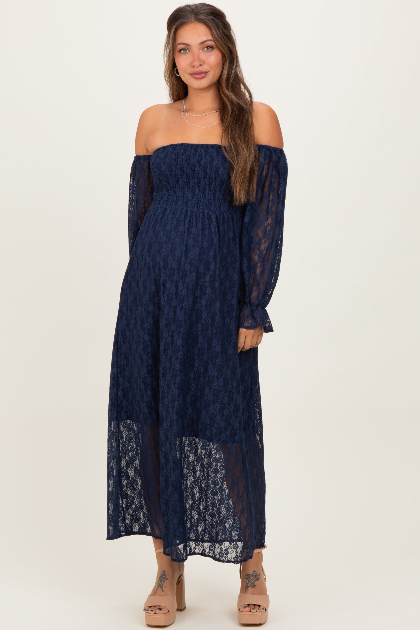 woman wearing a navy off-the-shoulder maternity dress with long sheer sleeves and a flowing silhouette, showcasing her baby bump
