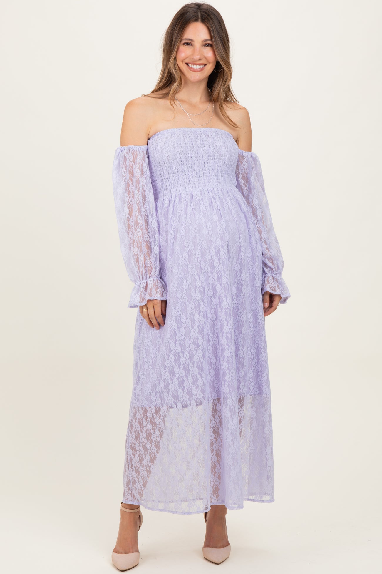 woman wearing a lavender off-the-shoulder maternity dress with long sleeves and a flowy skirt, showing her baby bump