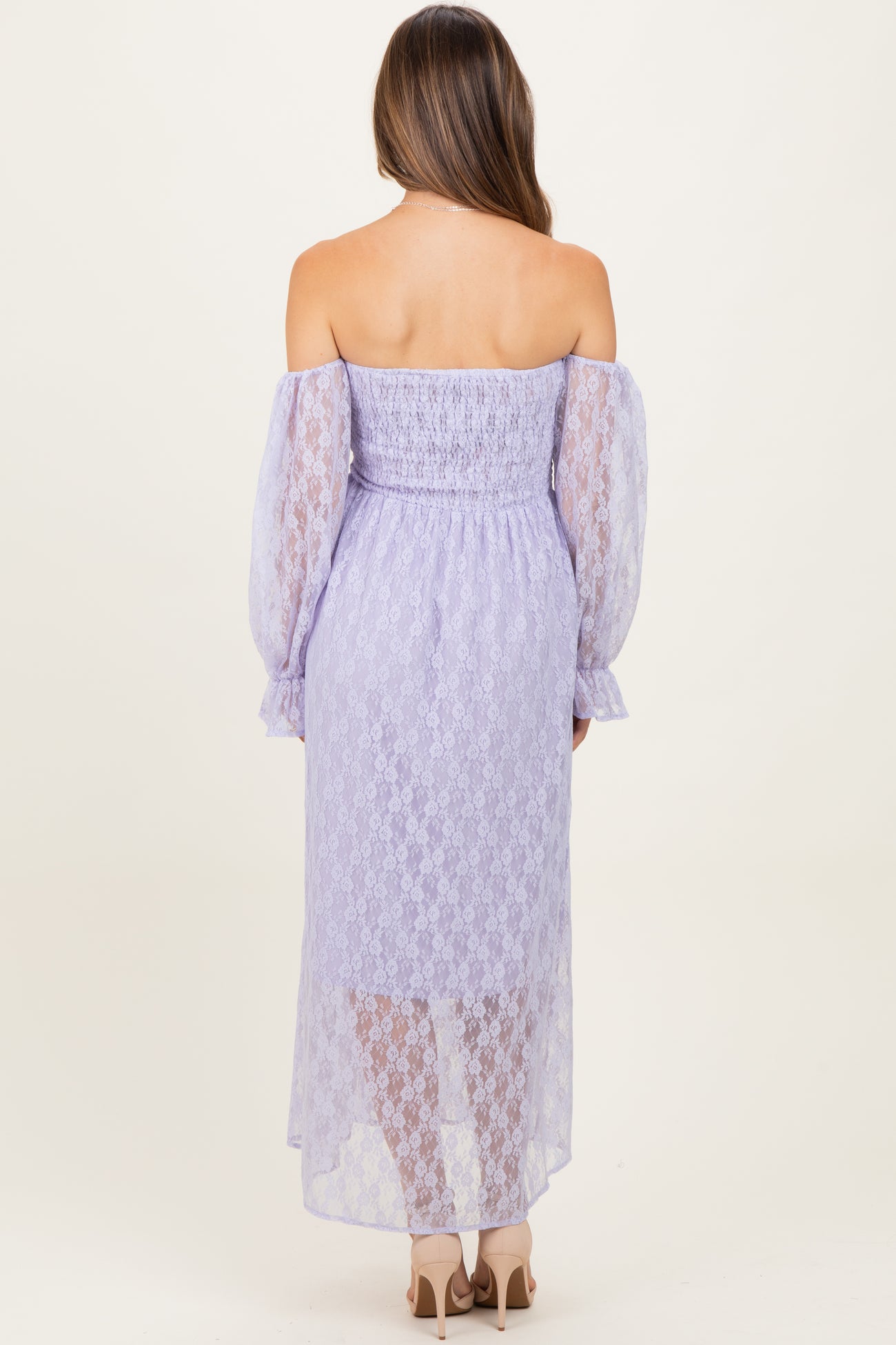 woman wearing a lavender off-the-shoulder maternity dress with lace details and long puff sleeves, showing her back