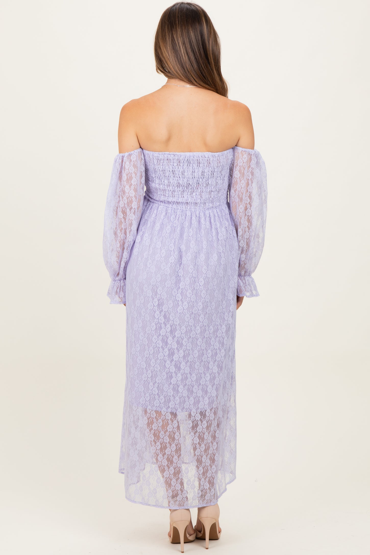 woman wearing a lavender off-the-shoulder maternity dress with lace details and long puff sleeves, showing her back